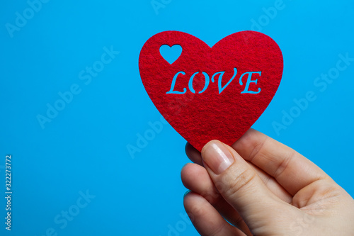 Decorative heart of red color with the inscription love in the hands of a man on a blue background