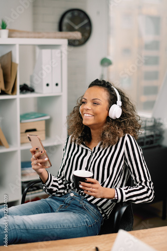 Young african businesswoman in office. Woman listening music and drinking coffee. 