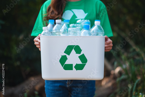 A woman collecting garbage and holding a recycle bin with plastic bottles in the outdoors