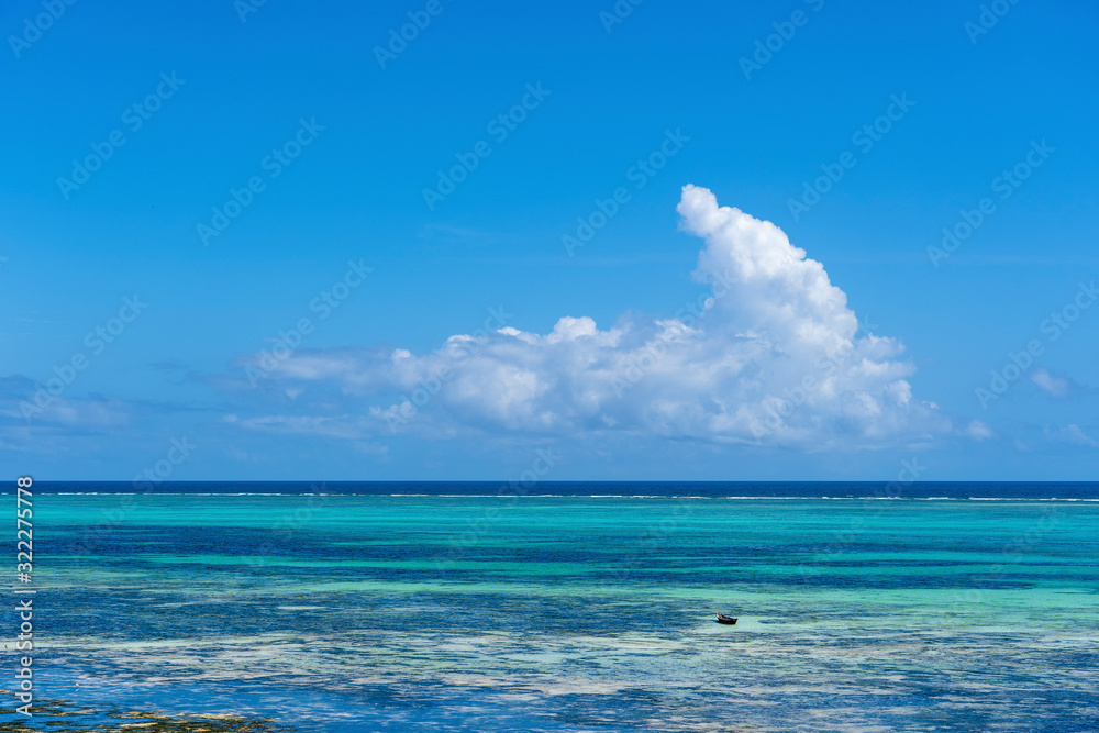 Obraz premium White beautiful clouds and blue sky over sea water waves on the island of Zanzibar, Tanzania, Africa. Travel and nature concept