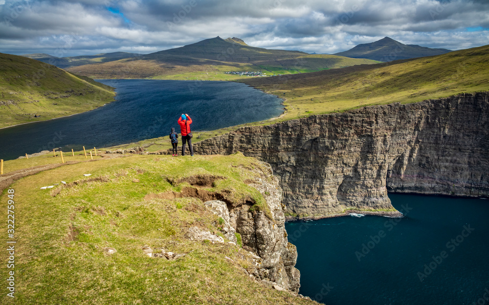 Tourists over Sorvagsvatn lake cliffs over the ocean under the clouds, Faroe Islands