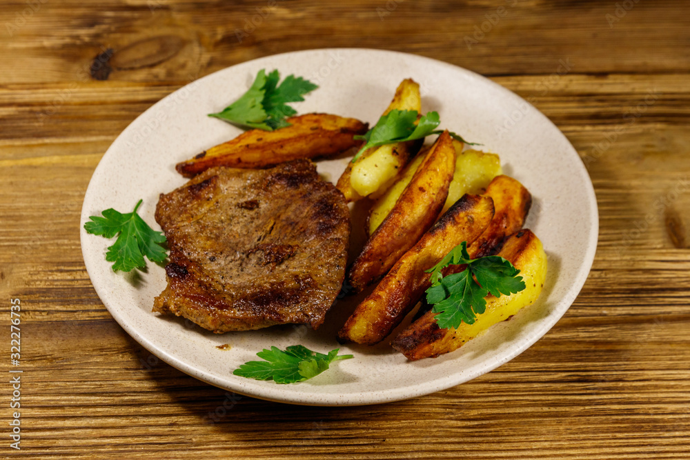 Fried beef steak with potato wedges on wooden table