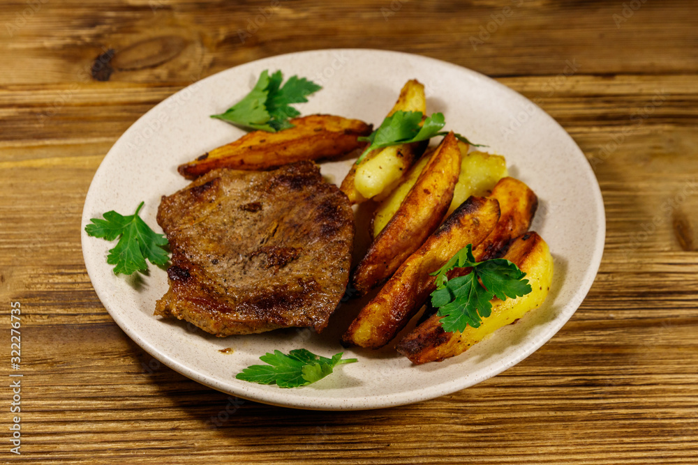 Fried beef steak with potato wedges on wooden table Fried beef steak with potato wedges on wooden table