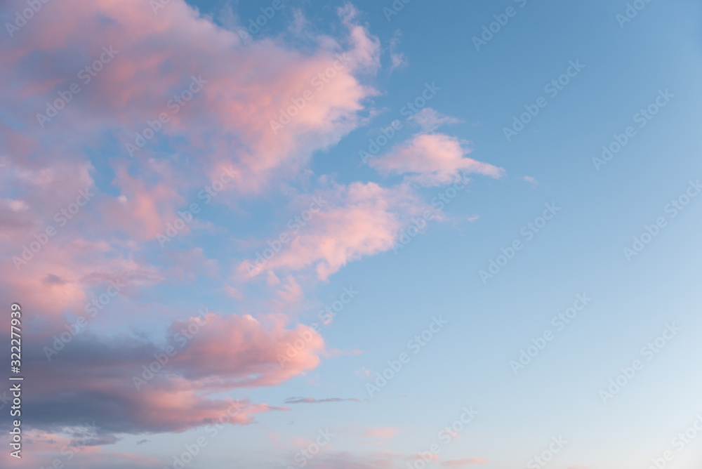 dreamy sky background, one half with fluffy pink clouds and blue side with copy space
