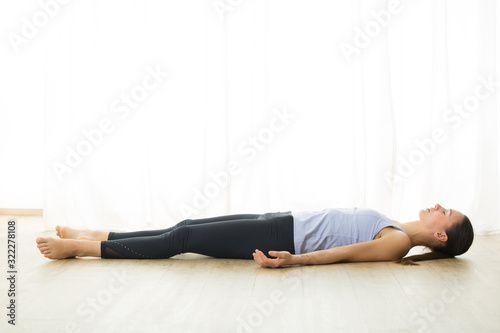 Portrait of gorgeous active sporty young woman practicing yoga in studio. Beautiful girl relaxing in Savasana, corpse pose. Healthy active lifestyle, working out indoors in gym. photo