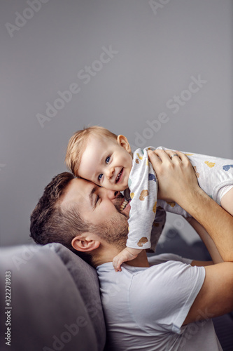 Young attractive caring father holding his beloved little son, singing song to him and having fun.