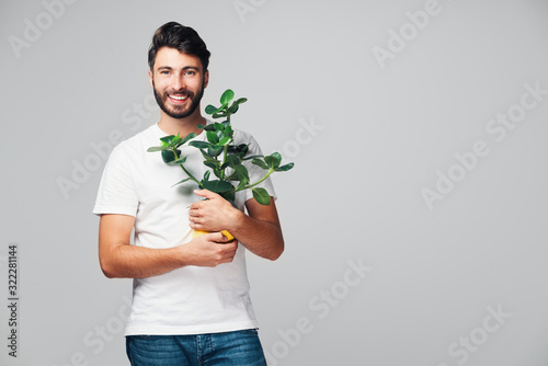 Handsome smiling millennial man holding plant isolated on grey background
