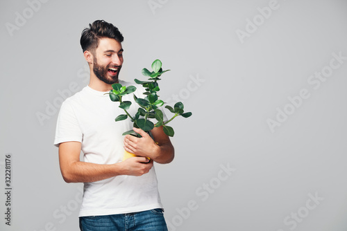 Handsome smiling young man holding potted plant isolated on grey background