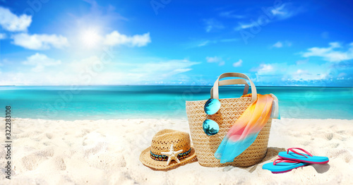 Fototapeta Naklejka Na Ścianę i Meble -  Concept summer holiday. Accessories - bag, straw hat, sunglasses with palm tree reflection, pareo, flip-flops on sandy beach against ocean, blue sky, clouds and bright sun. Beautiful colorful image.