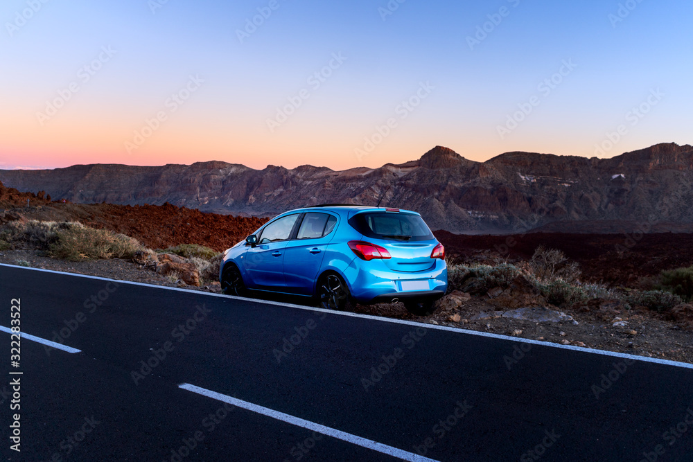 Tourism car on highway with sunset landscape. Blue car on the background of mountains.