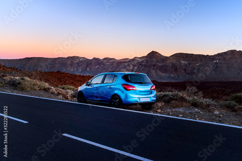 Tourism car on highway with sunset landscape. Blue car on the background of mountains.