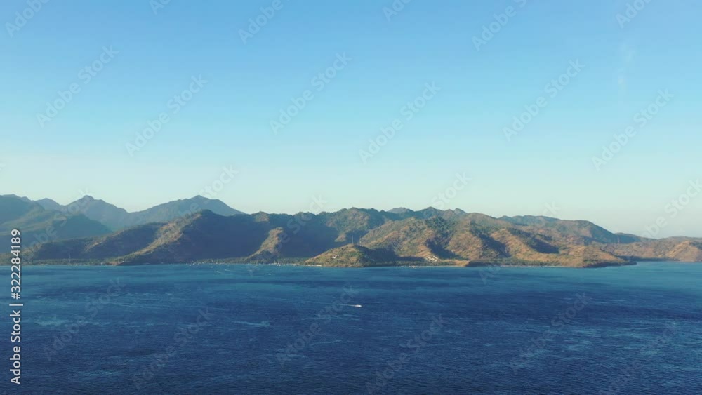 Volcanic mountains of Lombok, Indonesian islands under warm light of sunset, surrounded by deep blue sea on a bright sky background Volcanic mountains of Lombok, Indonesian islands under warm light of sunset, surrounded by deep blue sea on a bright sky background
