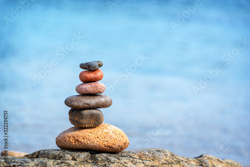 Fotografia Pile of pebbles on a beach, blue water background