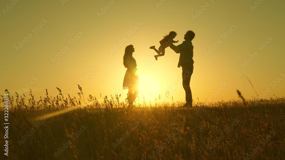 child, dad and mom play in meadow in the sun. concept of a happy childhood. mother, father and little daughter walking in a field in the sun. Happy young family. concept of a happy family.