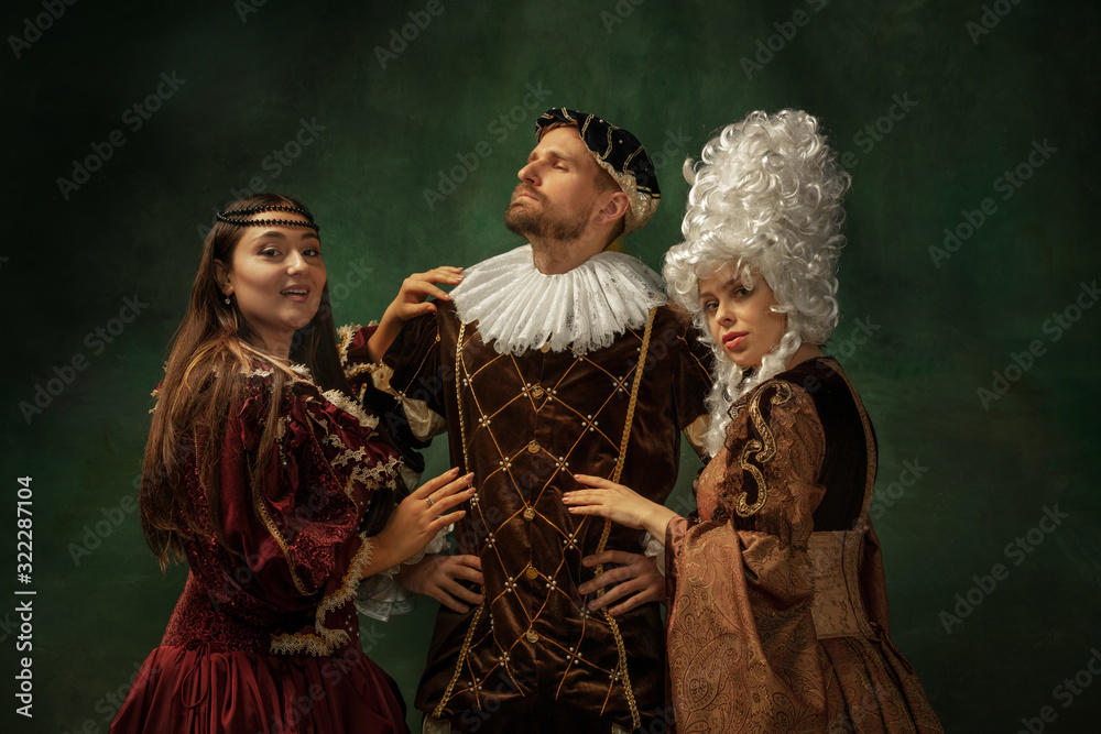 Love games pay attention. Portrait of medieval young people in vintage clothing on dark background. Models as a duke and duchess, princess, royal persons. Concept of comparison of eras, modern