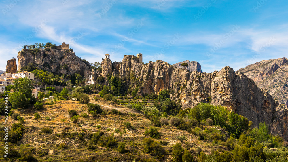 The beautiful medieval monastery of Guadalest with a castle and small towers in the mountains of the Spanish Costa Blanca. It is May, the sun is shining and some clouds are in the blue sky.