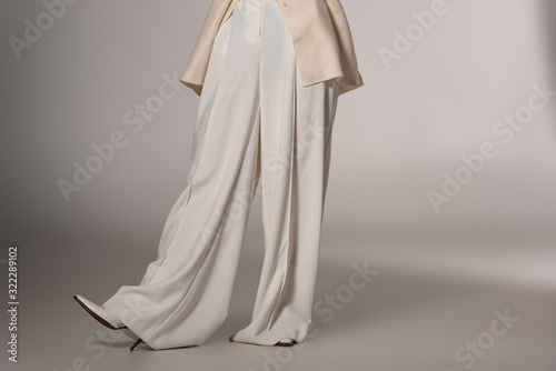 cropped view of stylish woman in white trousers on grey background
