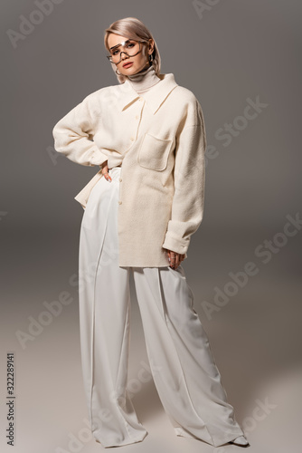 attractive woman in coat and trousers with hand on hip on grey background