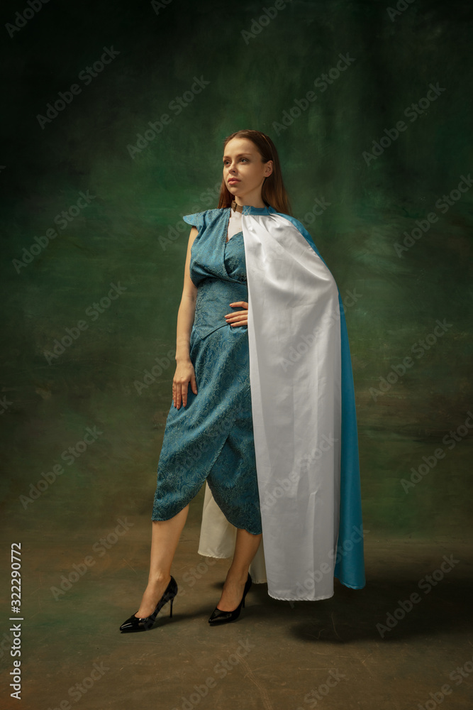 Elegance posing. Portrait of medieval young woman in blue vintage clothing on dark background. Female model as a duchess, royal person. Concept of comparison of eras, modern, fashion, beauty. Elegance posing. Portrait of medieval young woman in blue vintage clothing on dark background. Female model as a duchess, royal person. Concept of comparison of eras, modern, fashion, beauty.