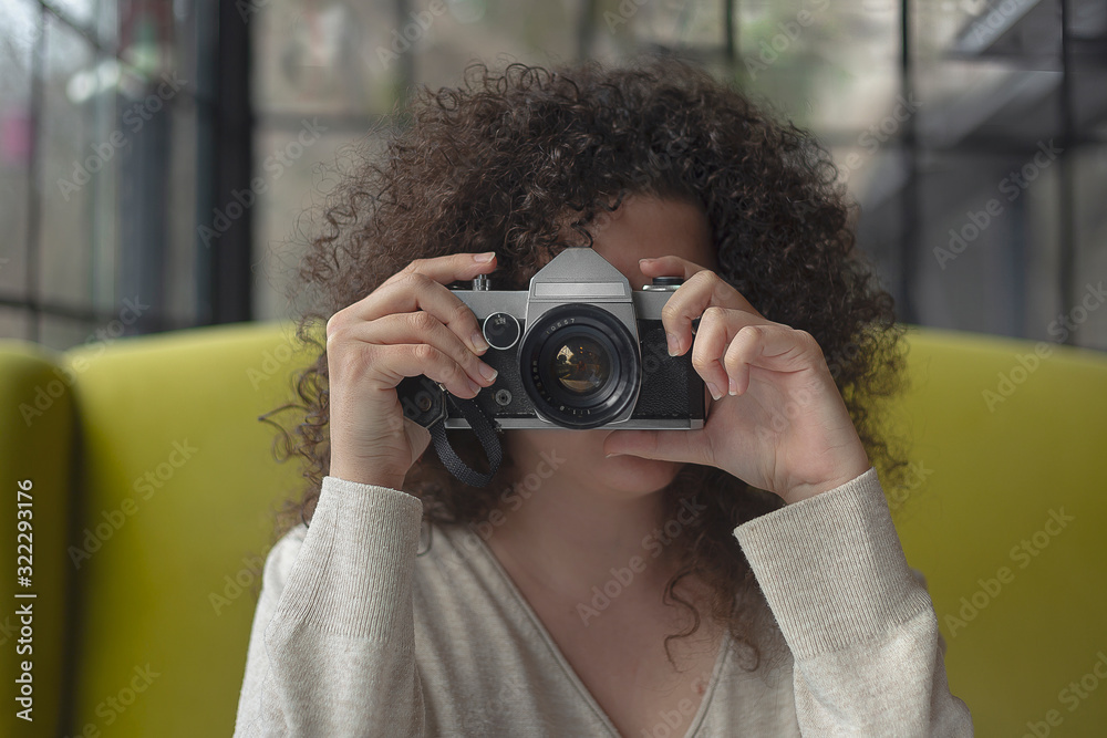 Curly haired photographer woman holding her camera in a cafe and shooting Curly haired photographer woman holding her camera in a cafe and shooting