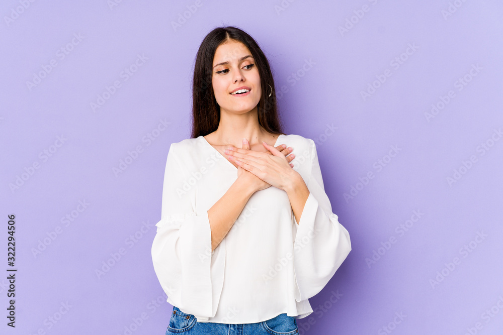 Young caucasian woman isolated on purple background has friendly expression, pressing palm to chest. Love concept. Young caucasian woman isolated on purple background has friendly expression, pressing palm to chest. Love concept.