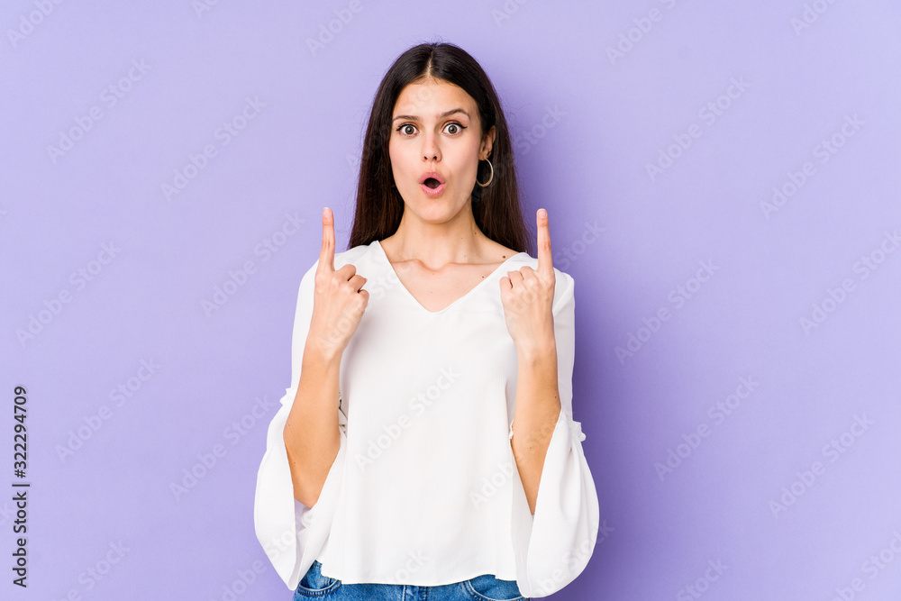 Young caucasian woman isolated on purple background pointing upside with opened mouth.