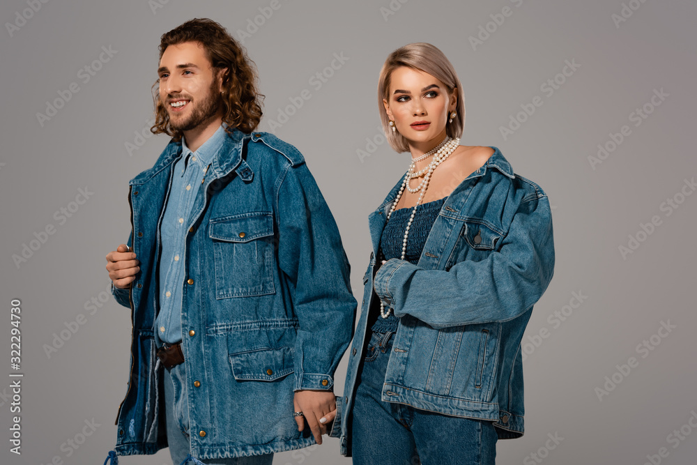 Fototapeta premium smiling man and woman in denim jackets holding hands isolated on grey