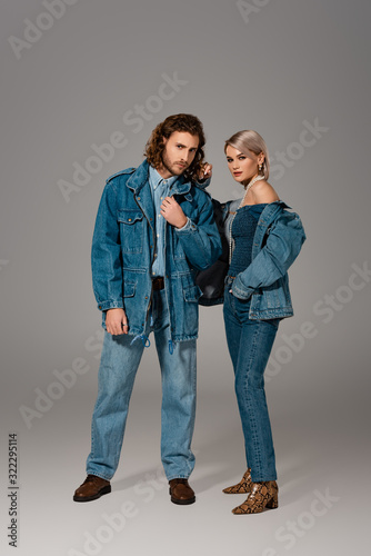 stylish man and woman in denim jackets and jeans looking at camera on grey background