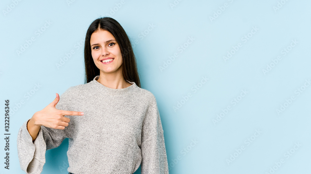 Fototapeta premium Young caucasian woman isolated on blue background person pointing by hand to a shirt copy space, proud and confident