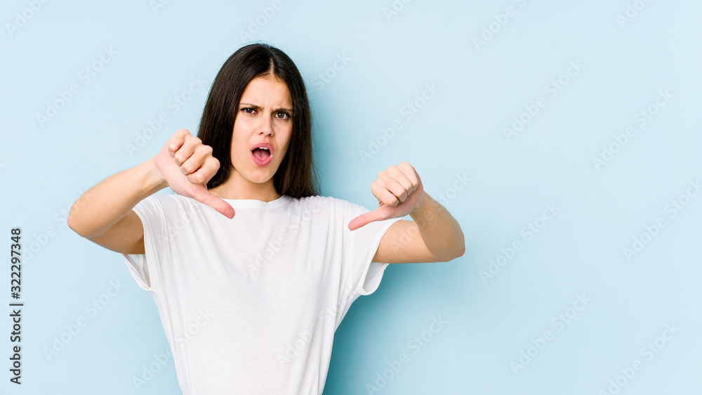 Young caucasian woman isolated on blue background showing thumb down and expressing dislike. Young caucasian woman isolated on blue background showing thumb down and expressing dislike.