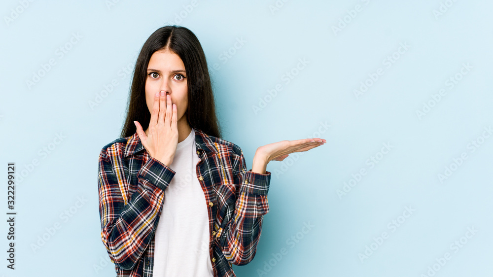 Young caucasian woman isolated on blue background impressed holding copy space on palm. Young caucasian woman isolated on blue background impressed holding copy space on palm.