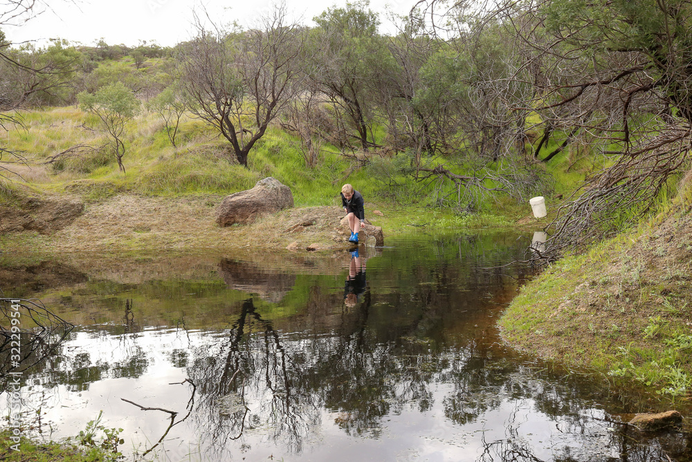 Young boy catching tadpoles in natural waterhole