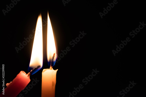 Meaningful image of Two Candles Lighting each other with black background for message and focus on orange candle. Concept of Celebration, Birthday, Homage, Tribute, Support and Help in difficult times