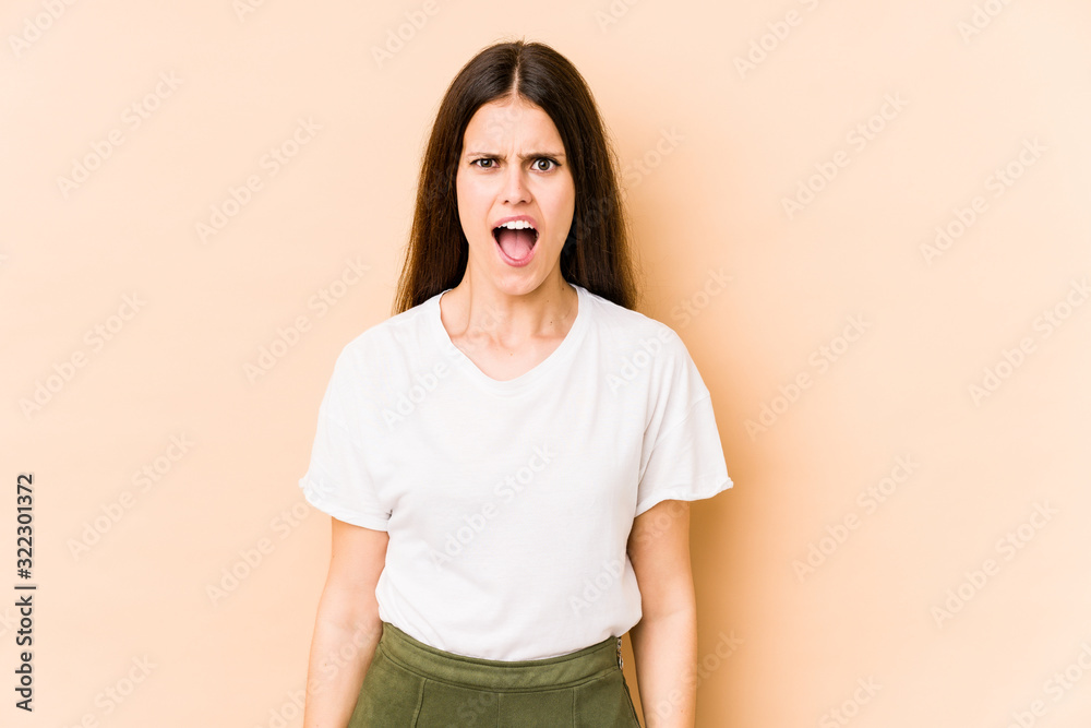 Young caucasian woman isolated on beige background shouting very angry, rage concept, frustrated.
