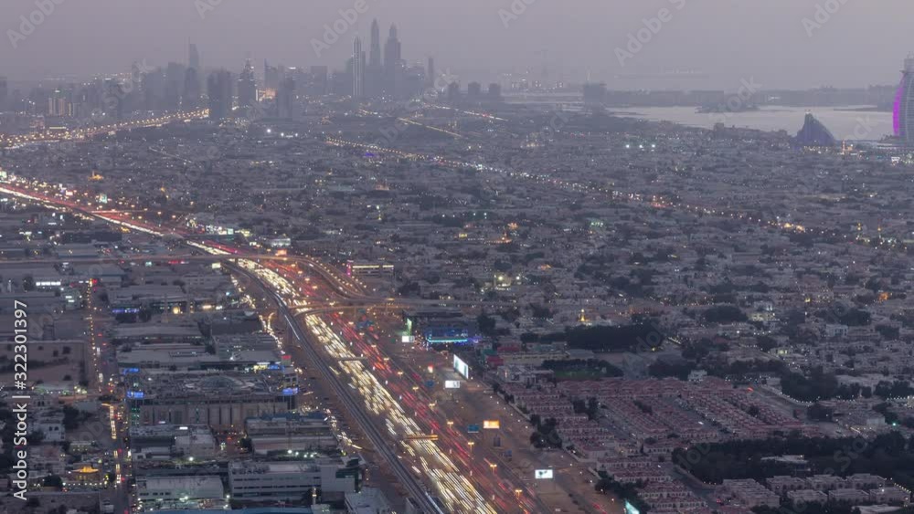 Aerial view to traffic on Sheikh Zayed road and intersection day to night transition timelapse, Dubai, United Arab Emirates. JLT and Dubai marina skyscrapers on a background. Metro line and houses. Aerial view to traffic on Sheikh Zayed road and intersection day to night transition timelapse, Dubai, United Arab Emirates. JLT and Dubai marina skyscrapers on a background. Metro line and houses.