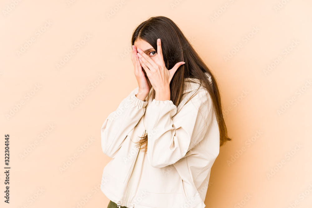 Young caucasian woman isolated on beige background blink through fingers frightened and nervous. Young caucasian woman isolated on beige background blink through fingers frightened and nervous.