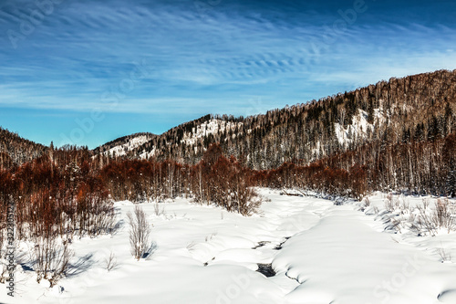 Beautiful winter landscape with a frozen river and forest-covered mountains on a Sunny winter day