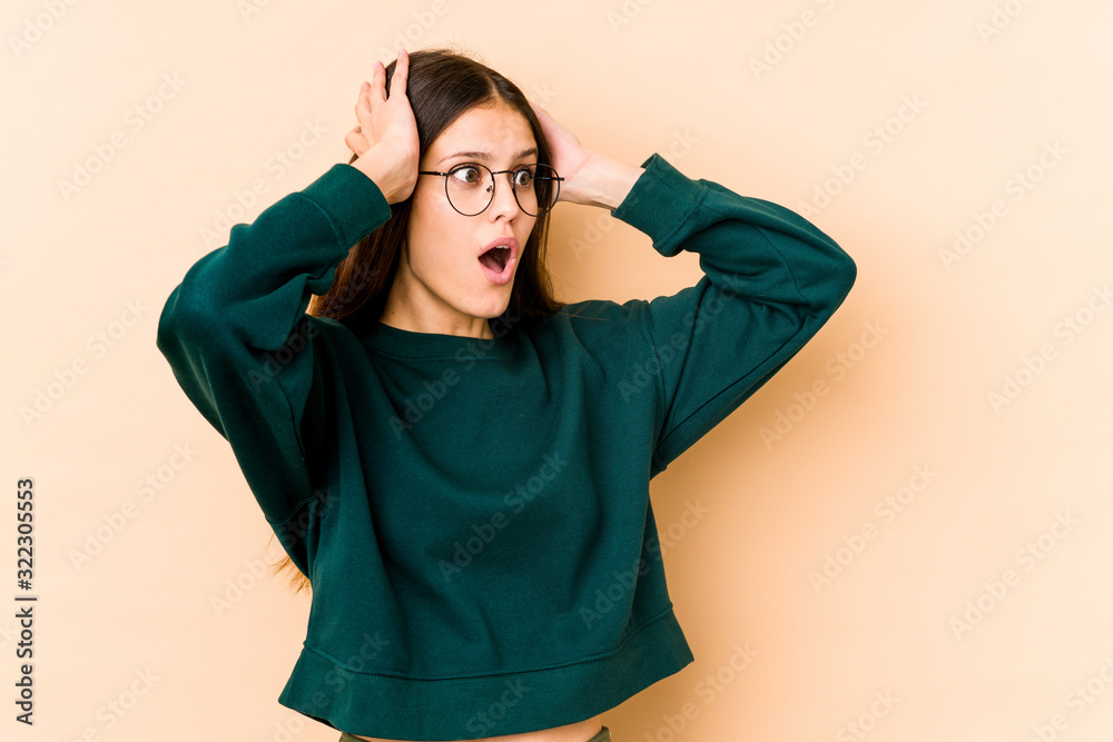 Young caucasian woman isolated on beige background screaming, very excited, passionate, satisfied with something.