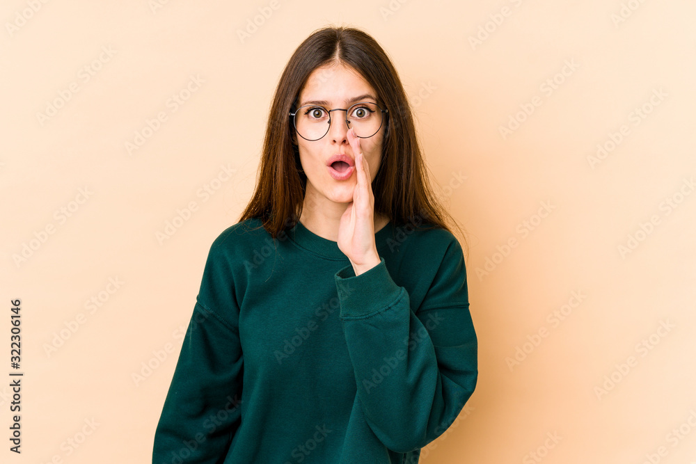 Fototapeta premium Young caucasian woman isolated on beige background is saying a secret hot braking news and looking aside