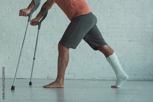 Side view of man with broken leg in gypsum holding crutches at home