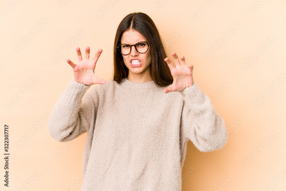 Young caucasian woman isolated on beige background showing claws imitating a cat, aggressive gesture. Young caucasian woman isolated on beige background showing claws imitating a cat, aggressive gesture.