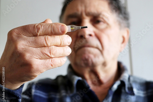 Elderly man measuring body temperature with mercury thermometer. Concept of fever, cold treatment, symptoms of coronavirus