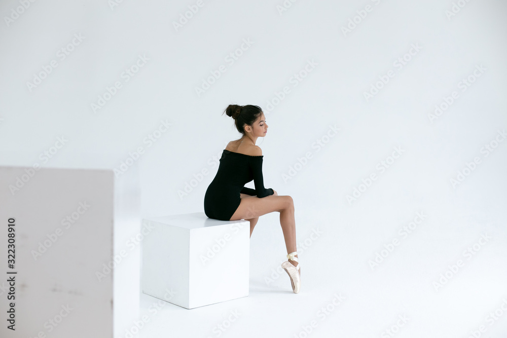 horizontal image of a ballerina sitting on a white cube in a white studio horizontal image of a ballerina sitting on a white cube in a white studio