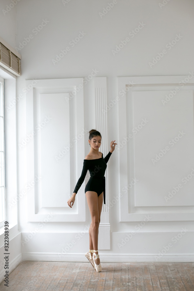 vertical photo of a young ballerina in a black leotard standing against a white wall vertical photo of a young ballerina in a black leotard standing against a white wall