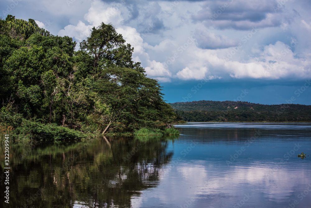 Reflection of lush vegetation in the waters of the Nile river. Blue horizon and clouds