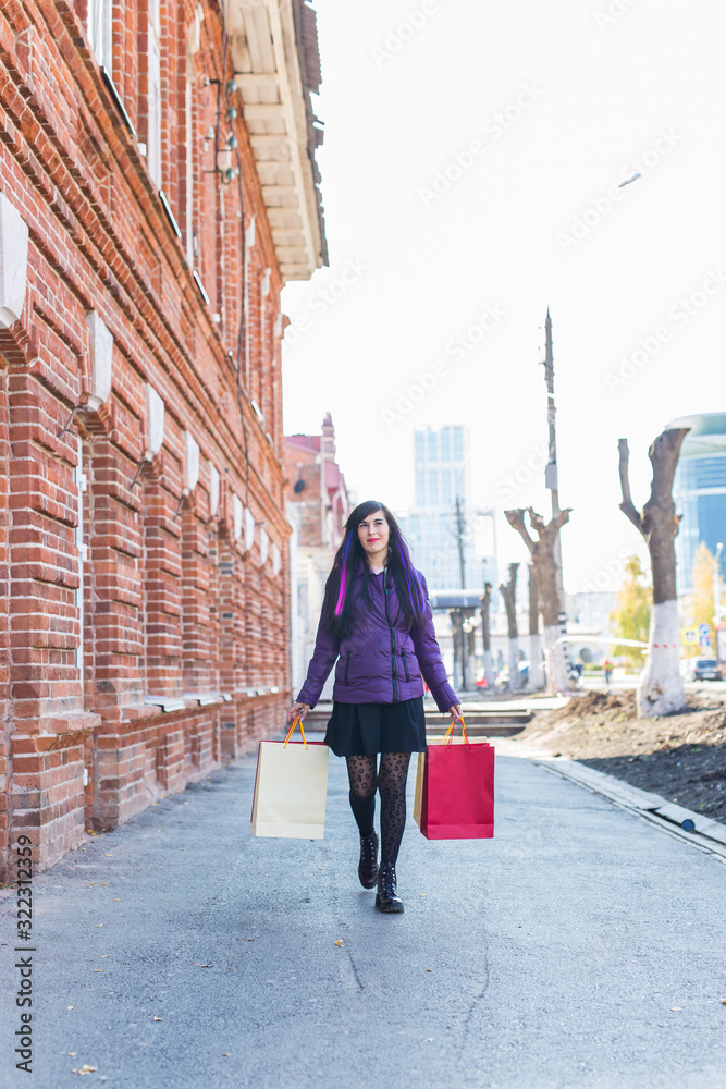 Fototapeta premium Shopping, consumer and sales concept - Beautiful woman holding many shopping bags on a city street