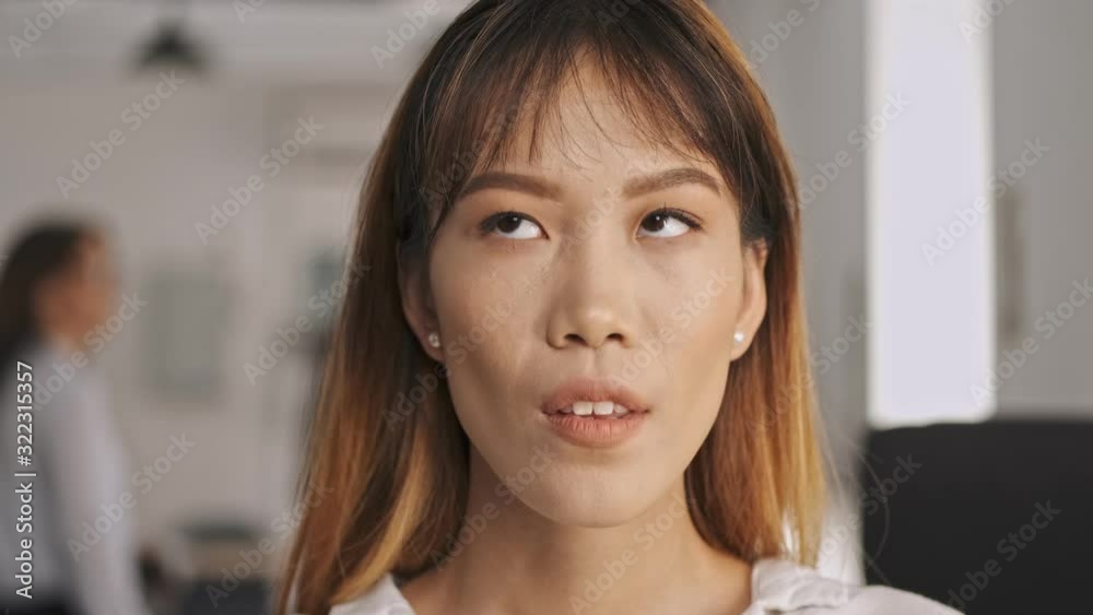 Close up view of Tired asian businesswoman sighing and rolling her eyes while standing in office Close up view of Tired asian businesswoman sighing and rolling her eyes while standing in office