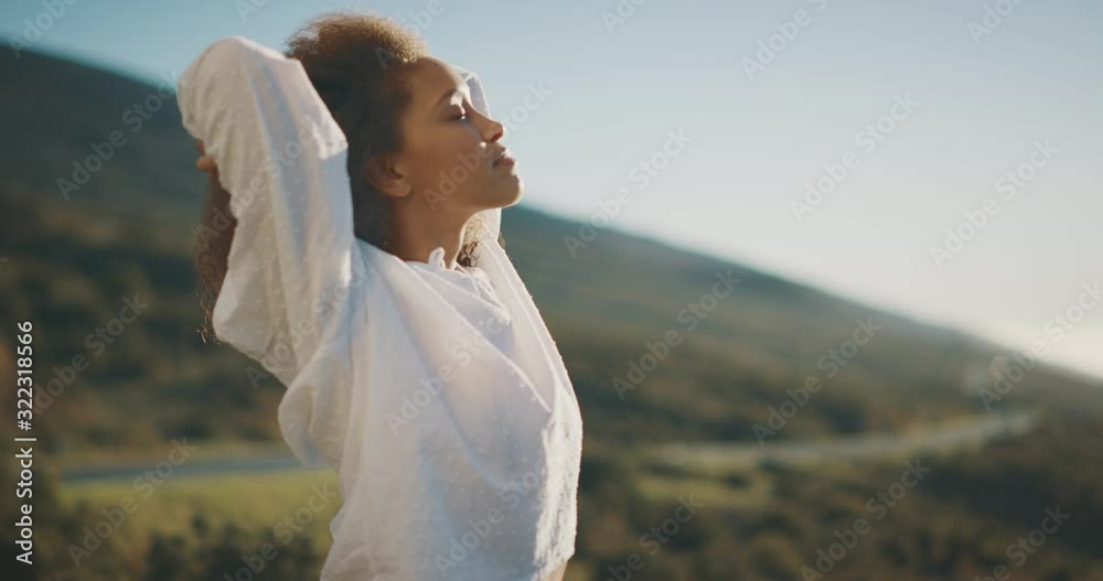 Young attractive african american woman raising her arms above her head and taking a relaxing deep breath outside, independent woman embracing life