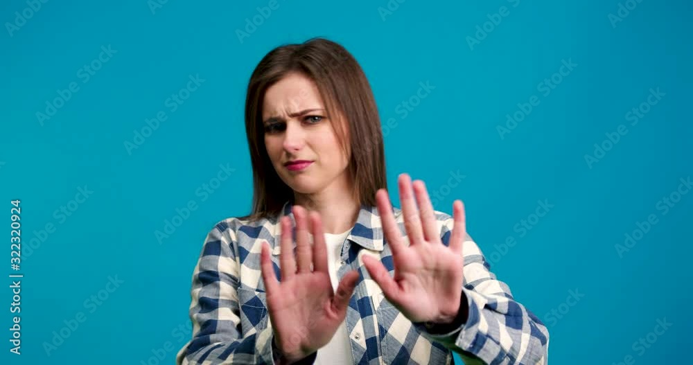Dissatisfied girl in checkered shirt shaking head and showing no gesture isolated on blue background Dissatisfied girl in checkered shirt shaking head and showing no gesture isolated on blue background