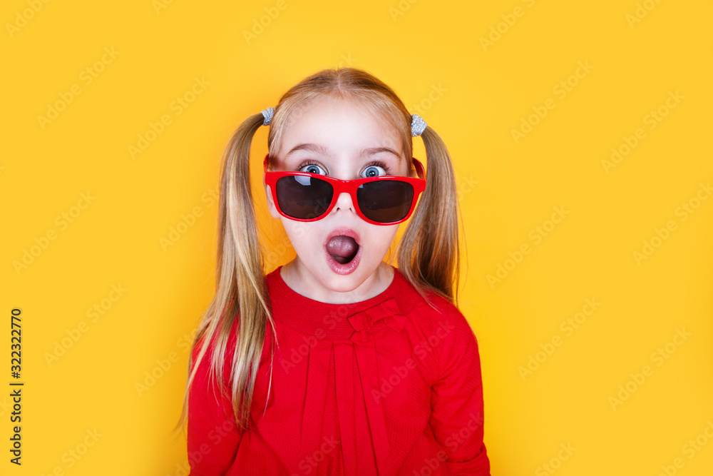 Shocked little girl in red sunglasses over yellow background - obrazy, fototapety, plakaty 